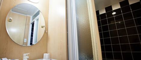 A bathroom with a round mirror, a sink, and a shower area.