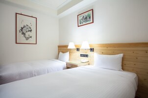 Una habitación de hotel con dos camas, un cabecero de madera, lámparas de noche, una mesita de noche con un teléfono y obras de arte enmarcadas en las paredes.