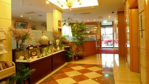 Un hall d’hôtel avec un sol à carreaux, un comptoir d’accueil et divers éléments décoratifs, notamment des vases et des plantes.