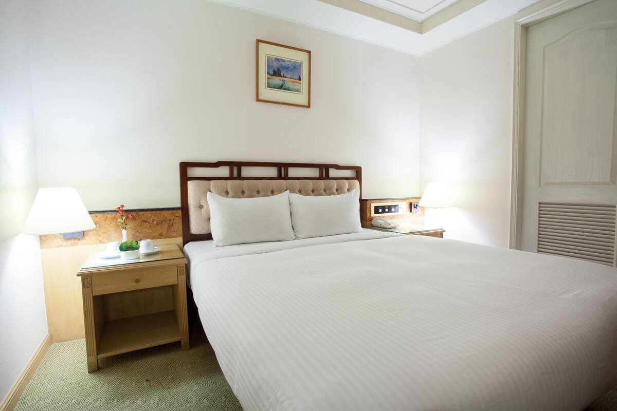Een hotelkamer met een groot bed, twee nachtkastjes met lampen, een klein bijzettafeltje en een lijst met een foto aan de muur.