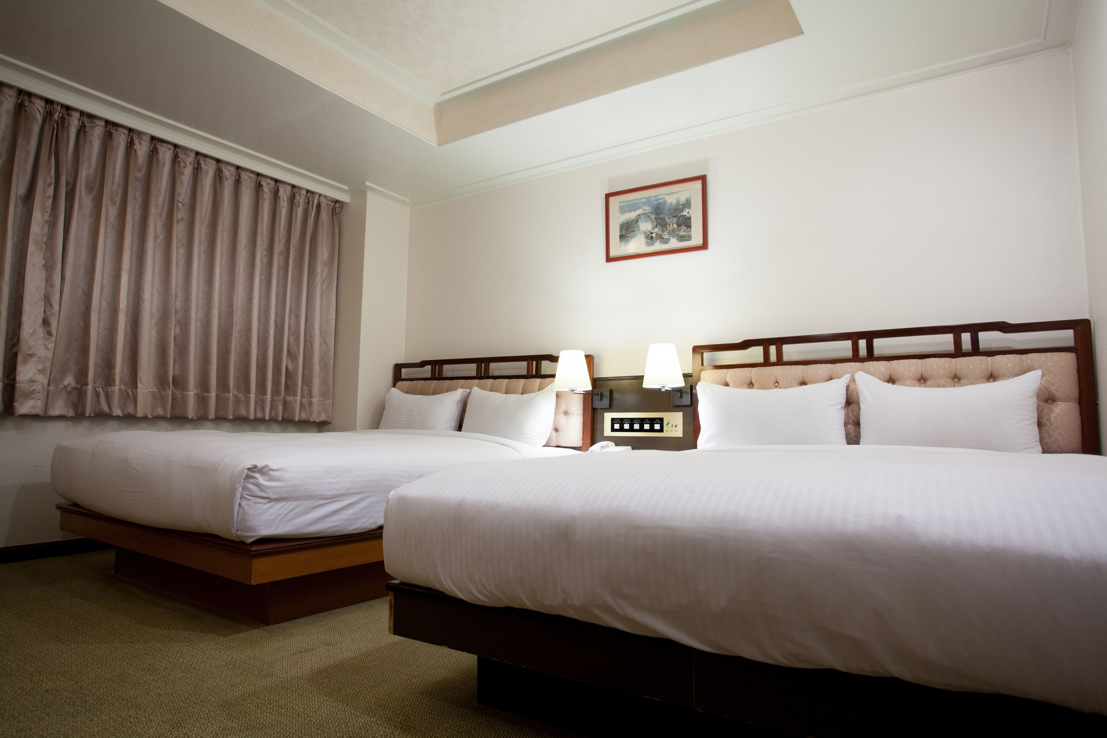 Habitación de hotel con dos camas, una mesita de noche con lámparas, un cuadro en la pared y una ventana con cortinas.