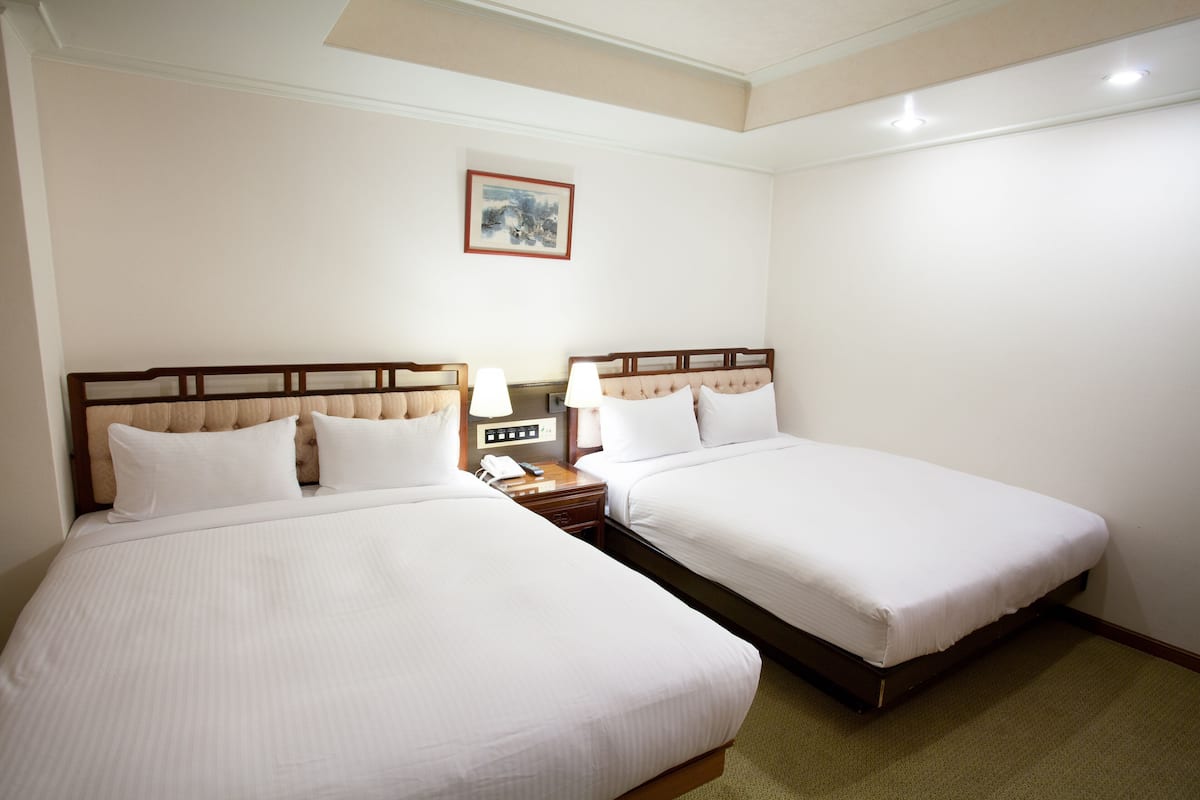 Een hotelkamer met twee bedden, een nachtkastje met een lamp en een ingelijst schilderij aan de muur.
