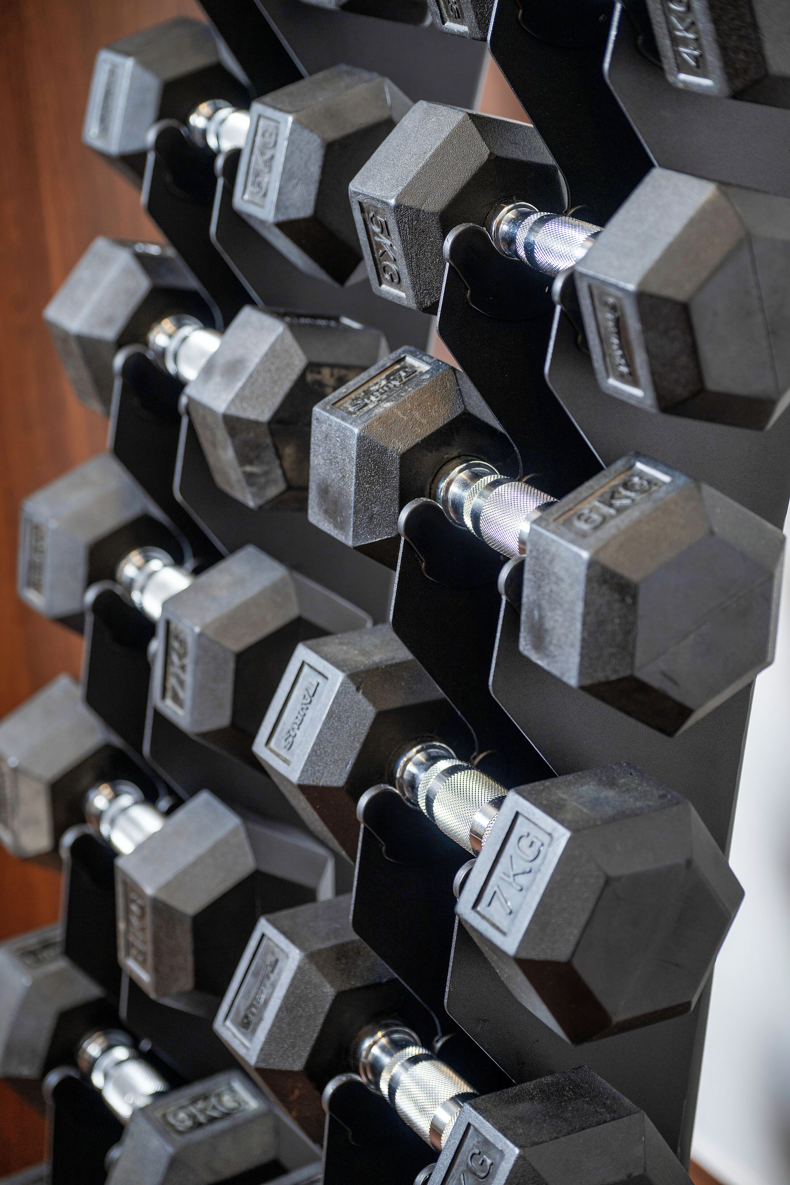 A rack of hexagonal dumbbells with weight labels, arranged in a vertical line.