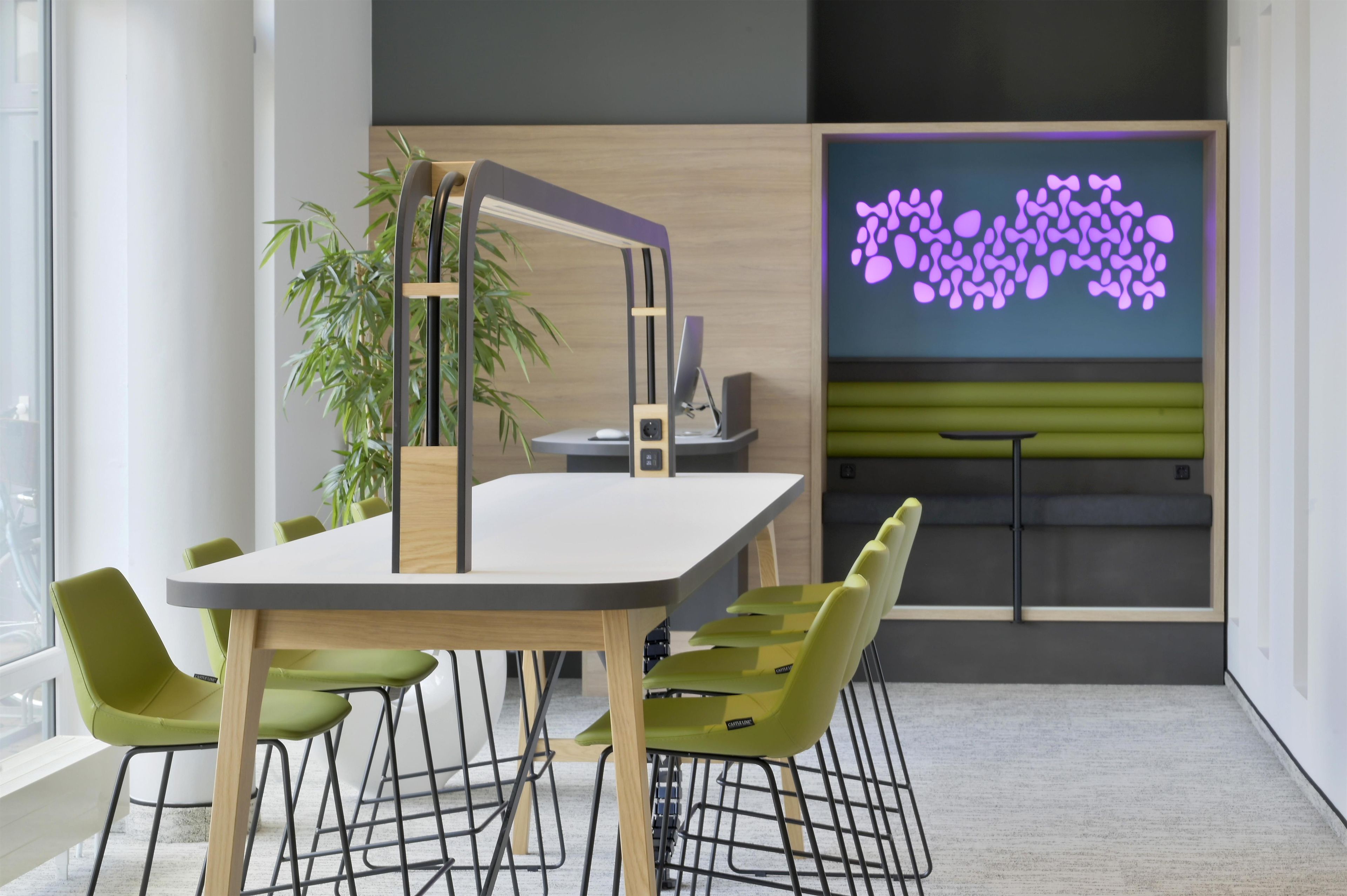 A modern office space with a white table, green chairs, a computer, and a decorative screen with purple patterns.