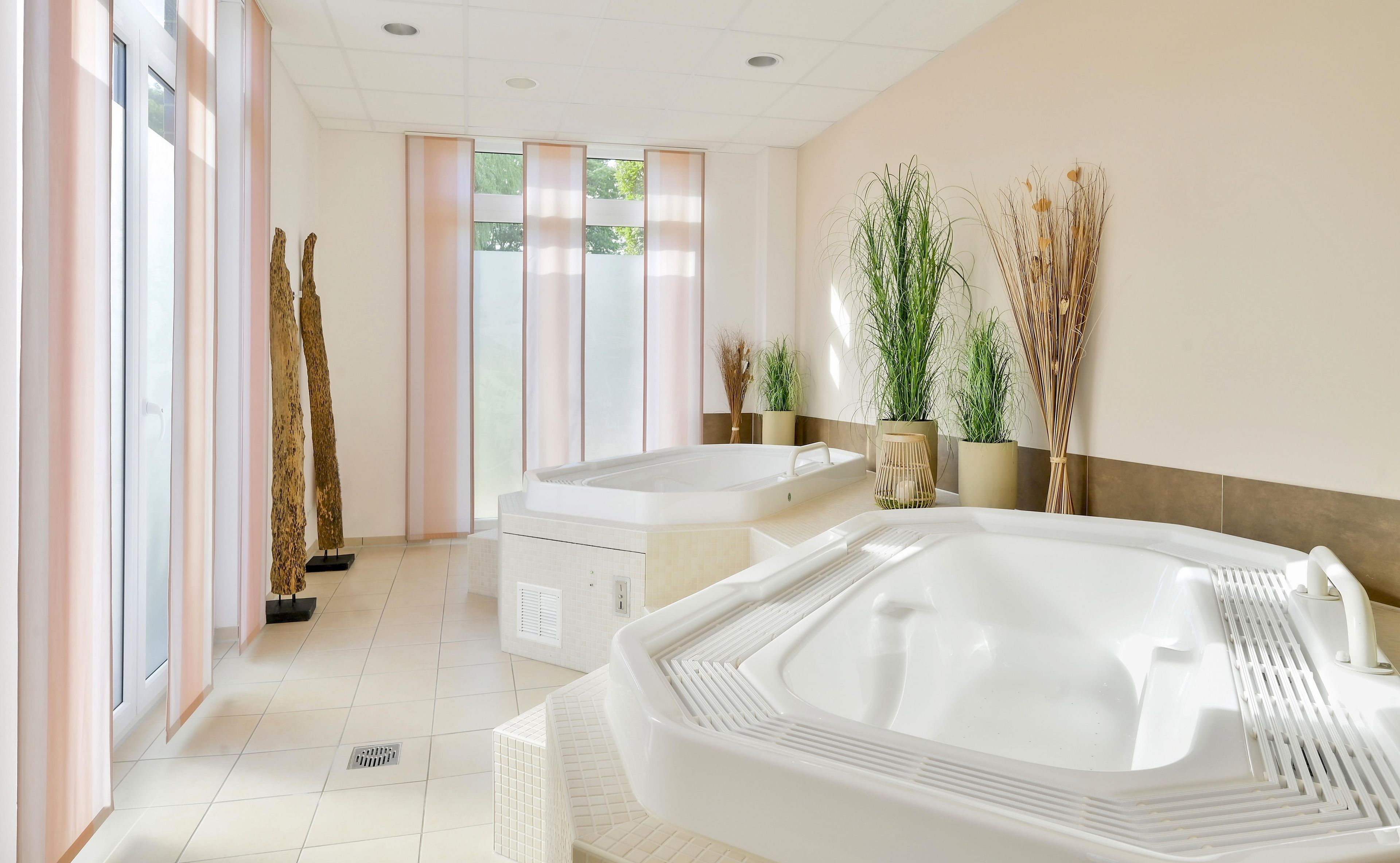 Een moderne badkamer met een groot bad, een douche en een toilet. Er staan potplanten en een decoratieve vaas op de muur.