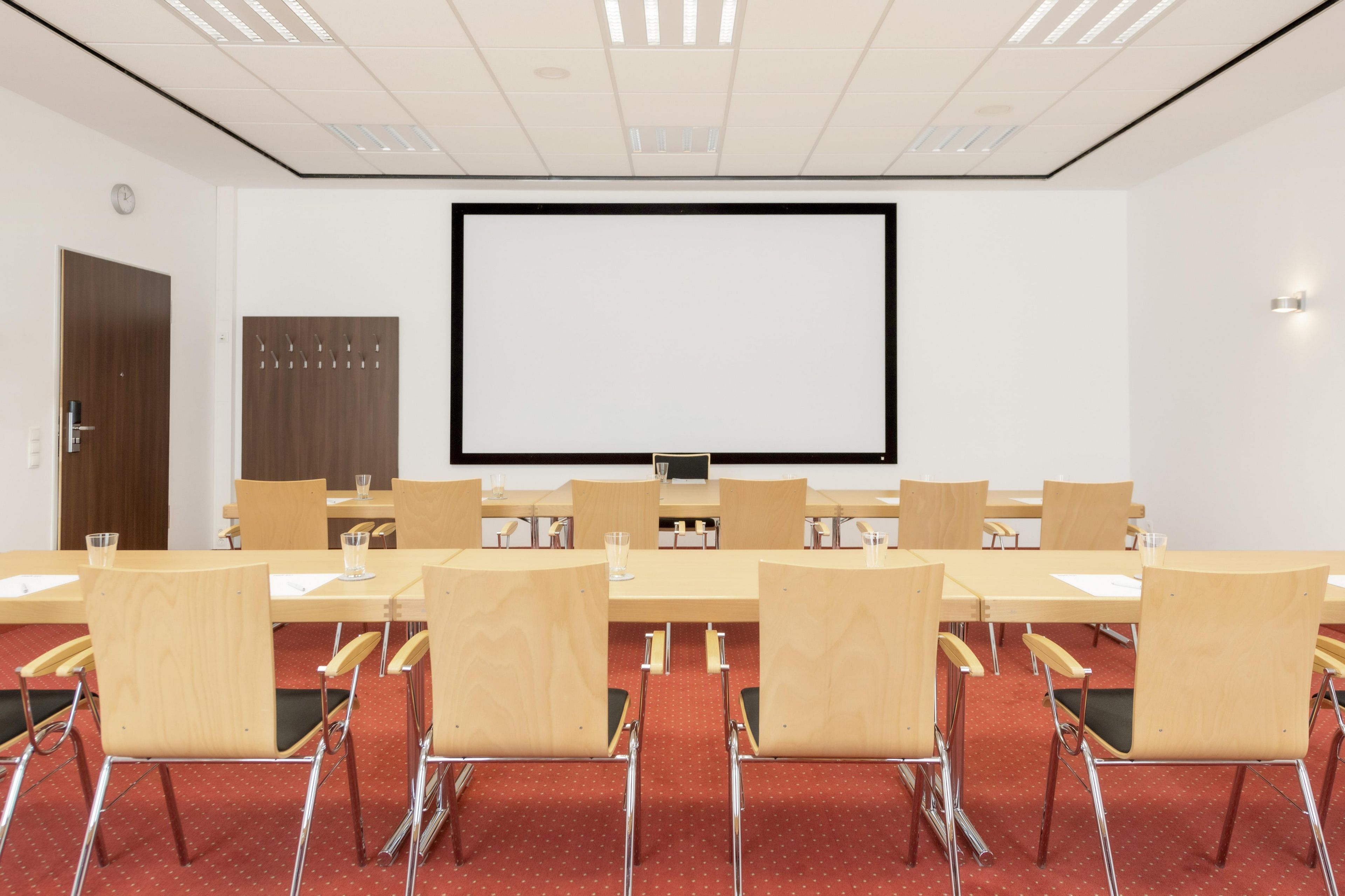 Un salón de conferencias con una pantalla grande, sillas de madera y mesas.