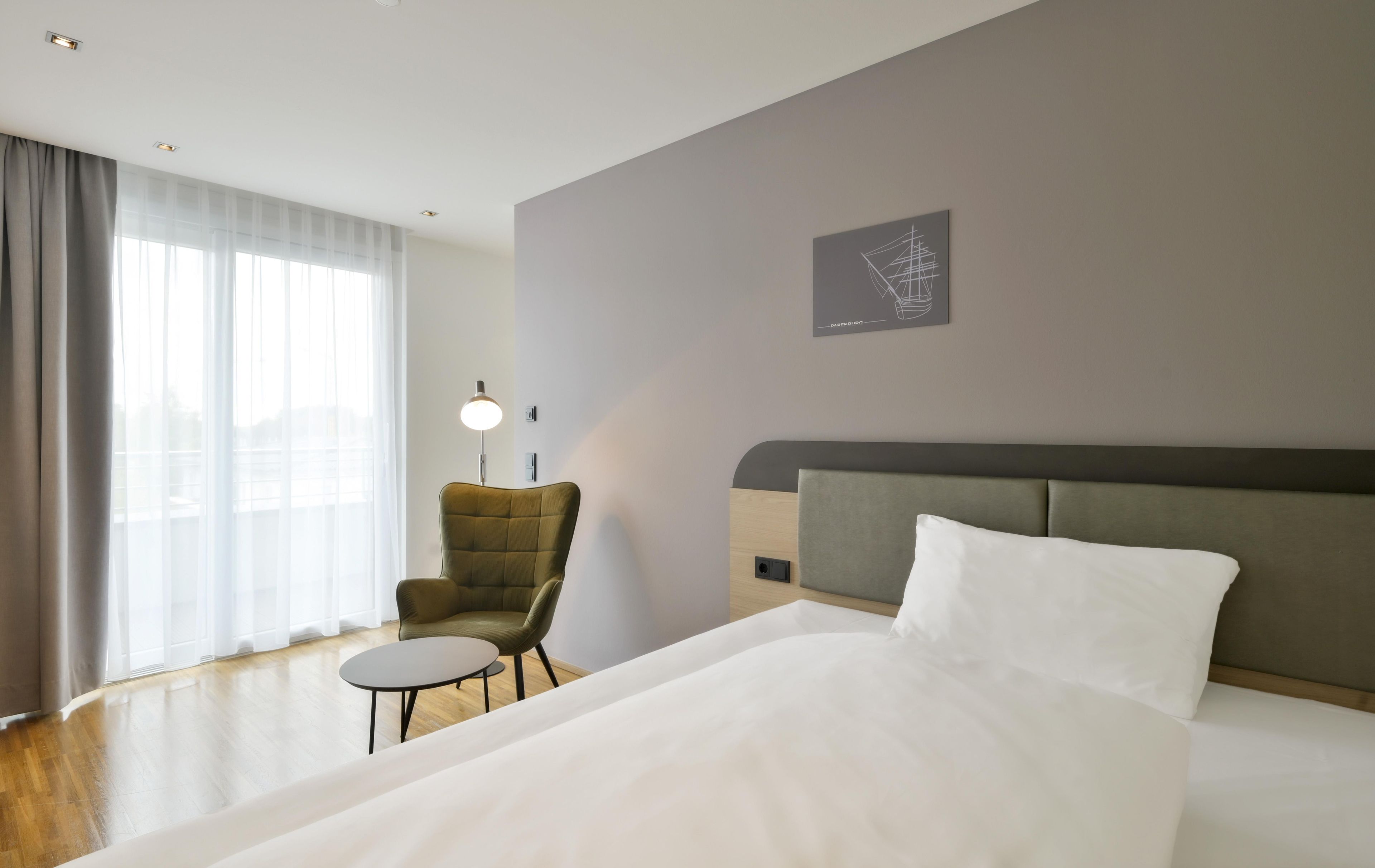 Une chambre d’hôtel avec un lit, une chaise, une petite table, une lampe et une œuvre d’art accrochée au mur.