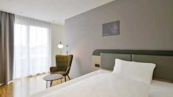 Une chambre d’hôtel avec un lit, une chaise, une petite table, une lampe et une œuvre d’art accrochée au mur.