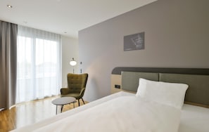 Ein Hotelzimmer mit einem Bett, einem Sessel, einem kleinen Tisch, einer Lampe und einem Wandbild.