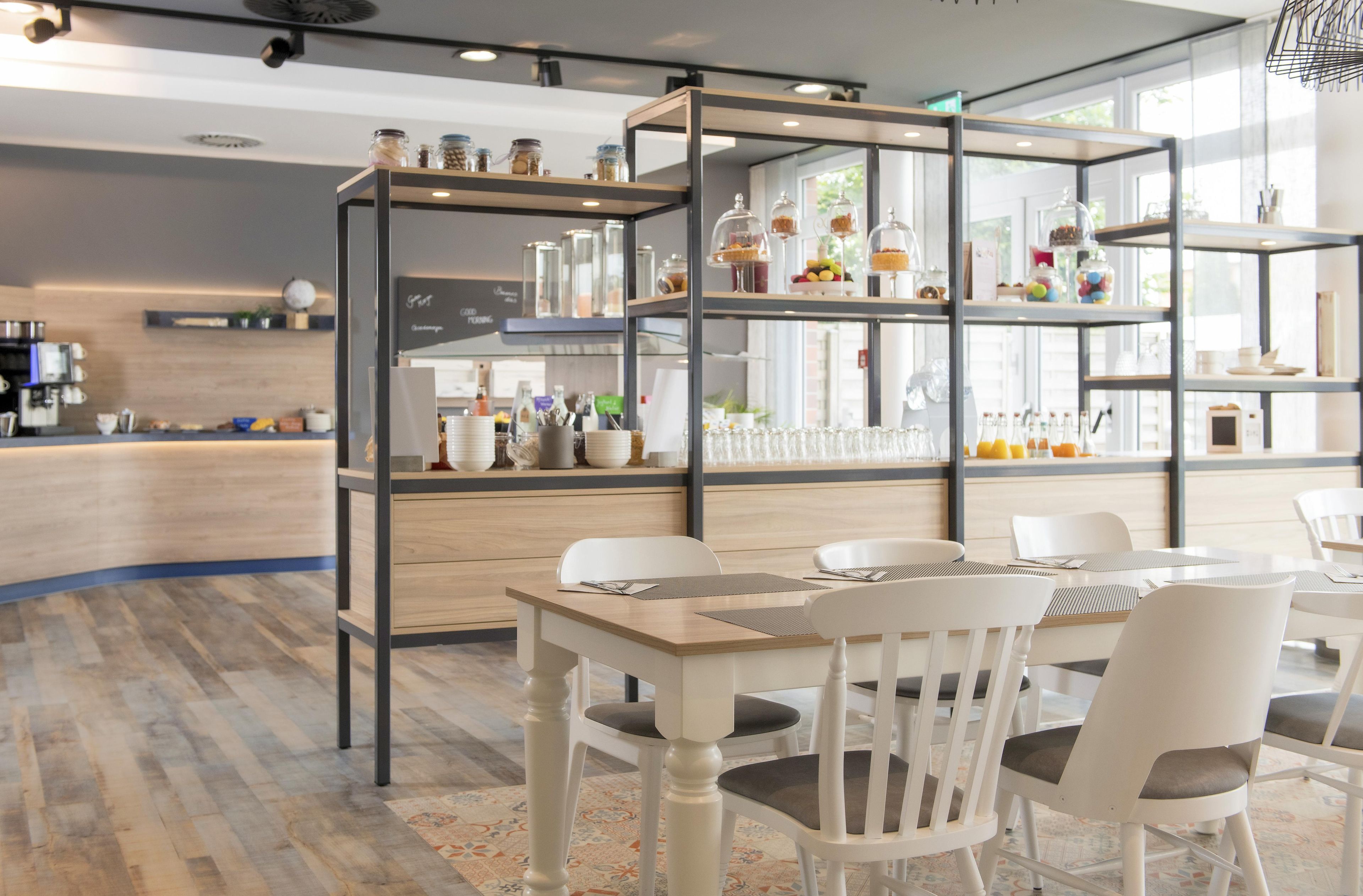 A modern cafe interior with a wooden counter, white chairs, and a glass display case with food items.