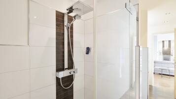 A modern bathroom with a glass shower enclosure, a handheld showerhead, and a wall-mounted faucet.