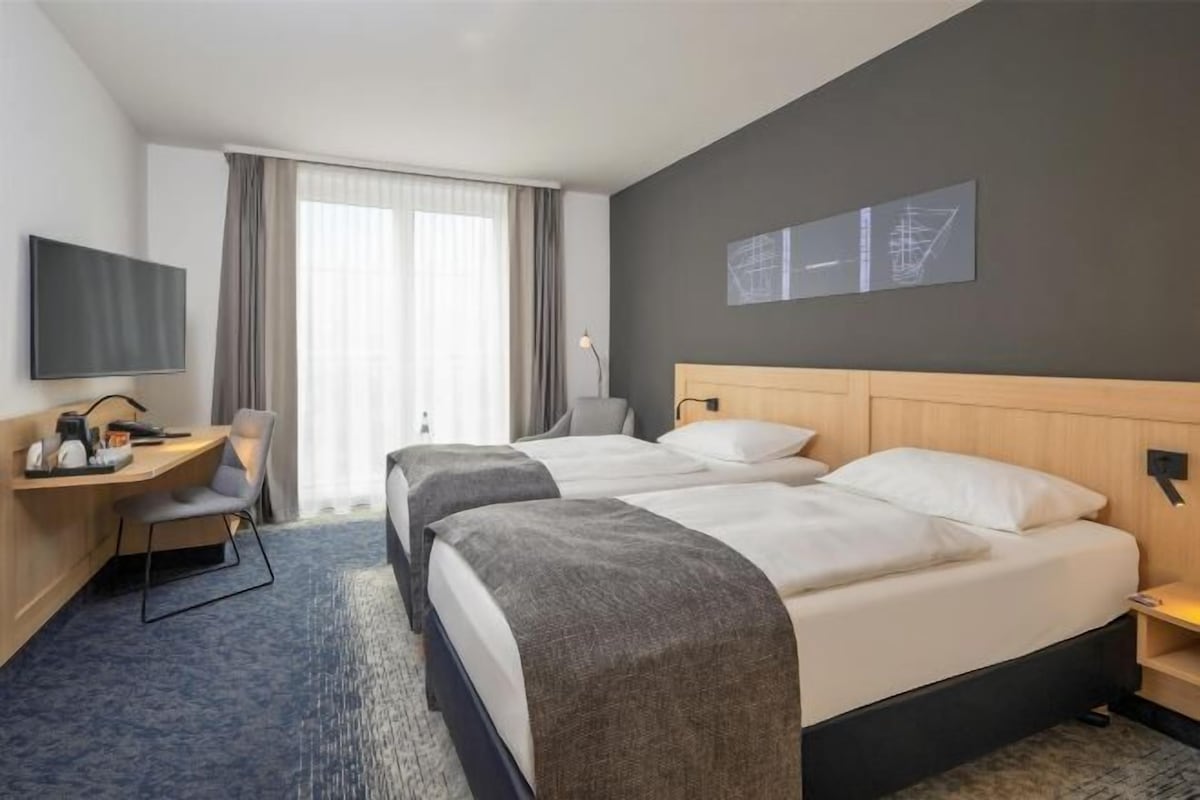 A hotel room with two beds, a desk, a chair, a TV, and a window with curtains.