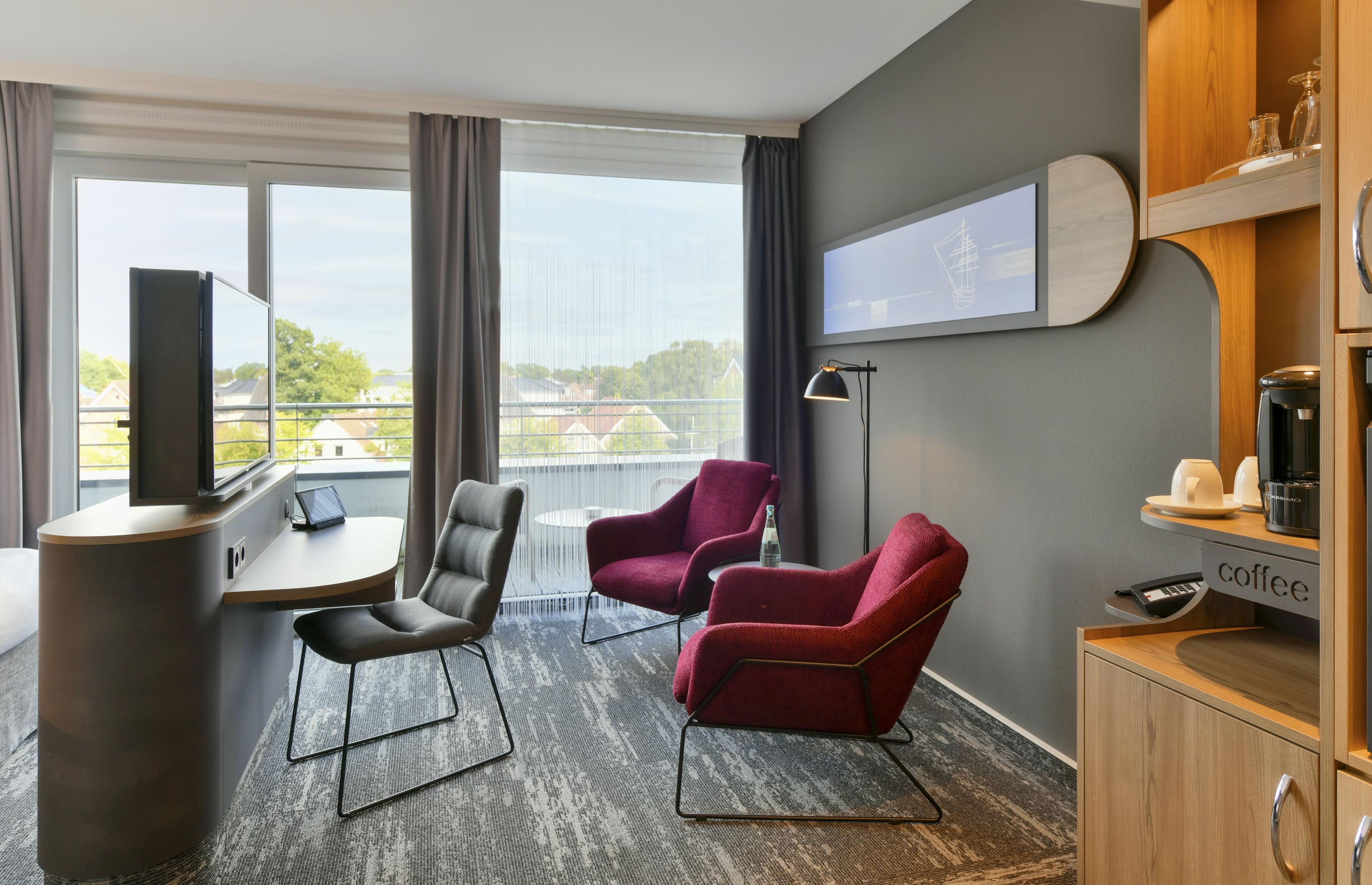 A hotel room with a desk, two chairs, a coffee station, and a large window with a view.