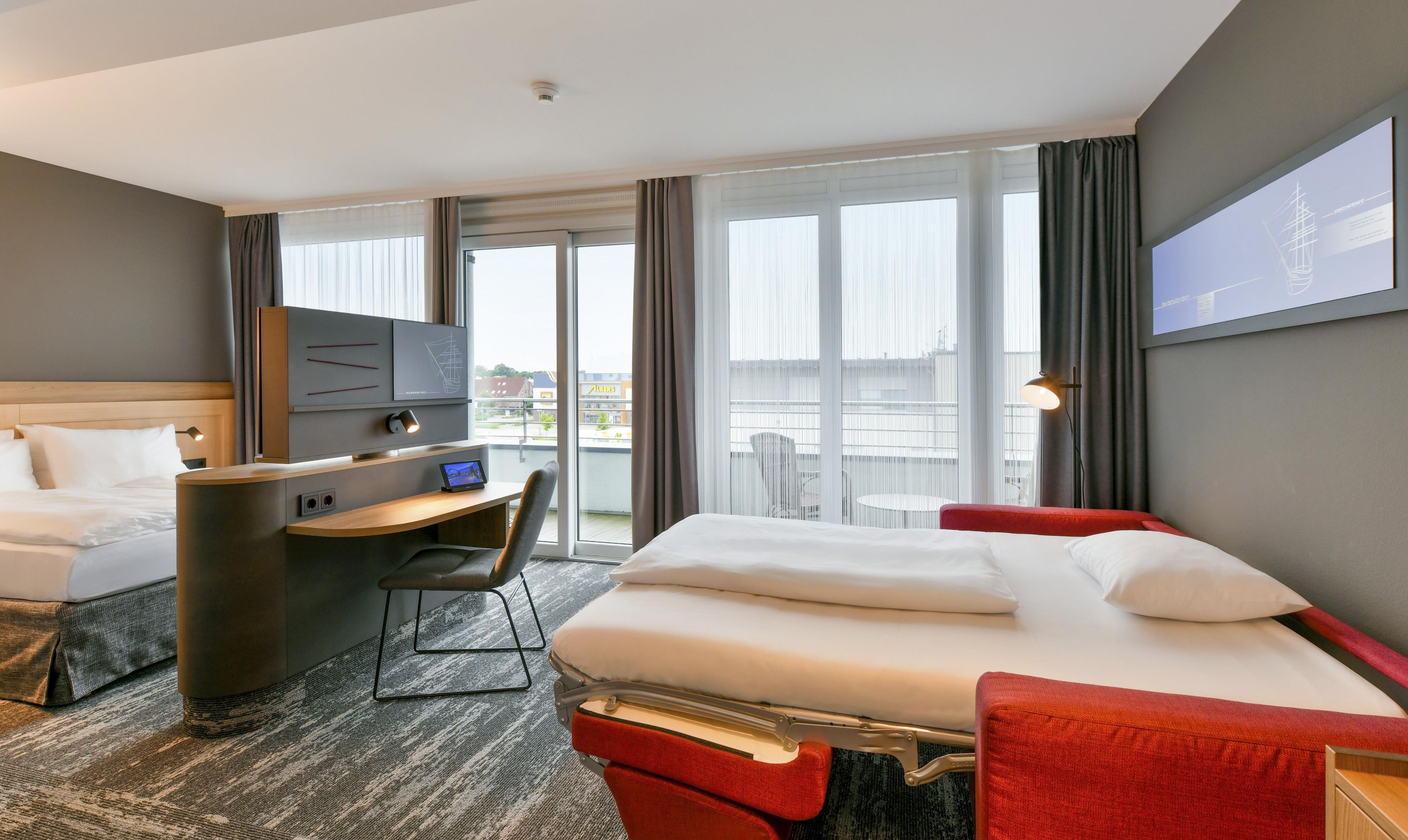 A hotel room with a bed, a desk, a chair, a television, and a balcony with curtains.
