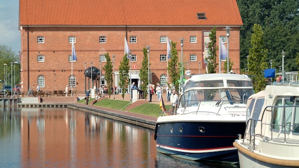 A brick building with a red roof, a canal with boats, and people near the entrance. - Best Western Plus Hotel Papenburg (Papenburg)