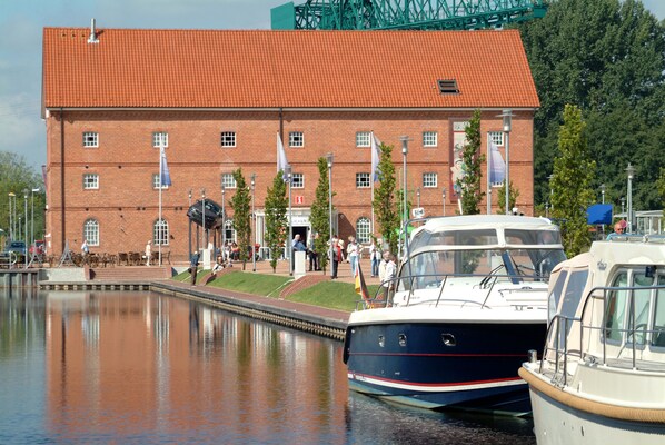 A brick building with a red roof, a canal with boats, and people near the entrance. - Best Western Plus Hotel Papenburg (Papenburg)