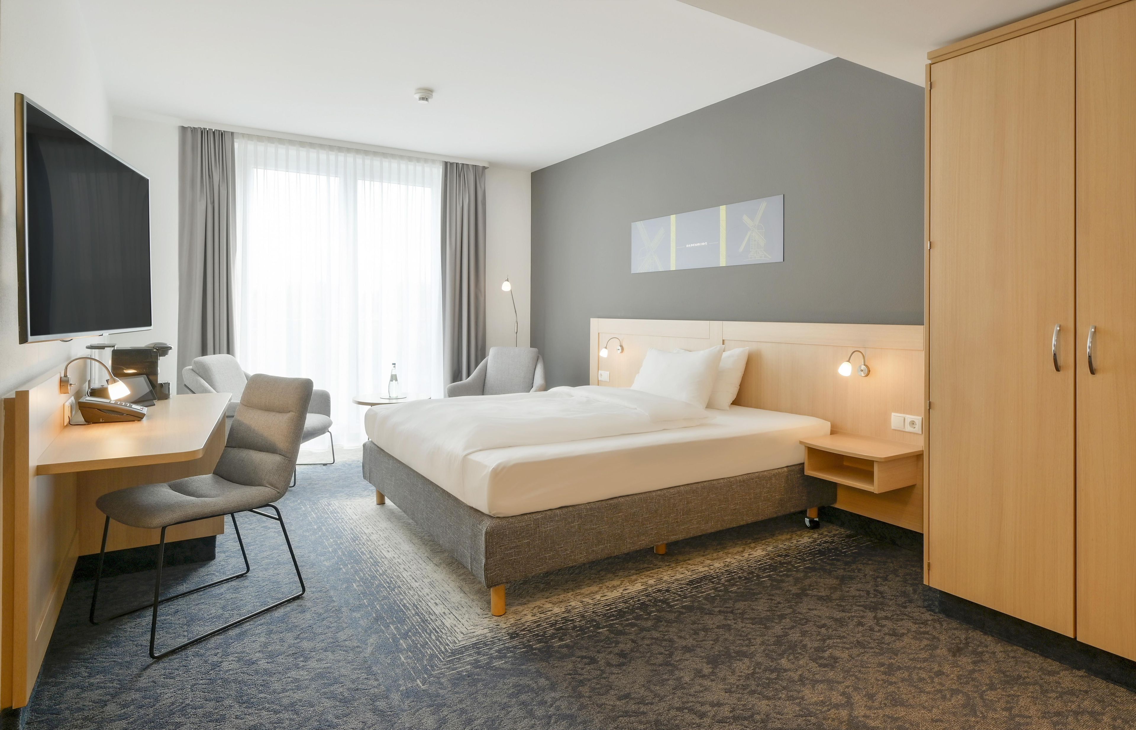 Een hotelkamer met een bed, bureau, stoel en kledingkast.