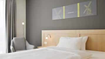 Une chambre d’hôtel avec un lit, une chaise, une lampe fixée au mur et un tableau.
