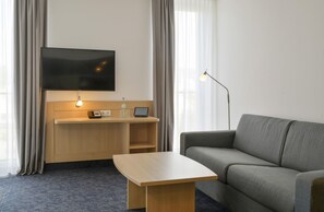A hotel room with a sofa, a desk with a flat-screen TV, a lamp, and a table. - Best Western Plus Hotel Papenburg (Papenburg)
