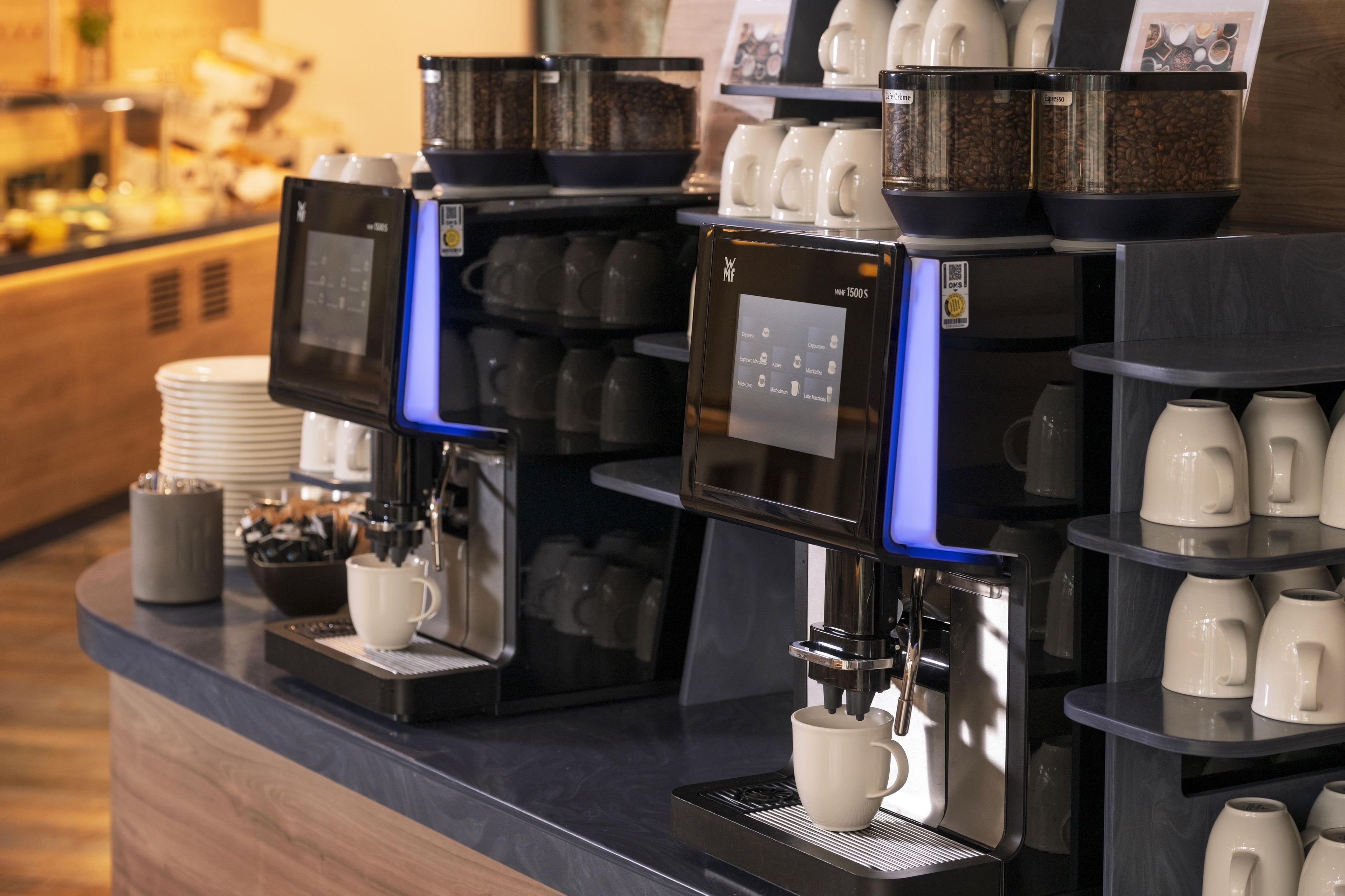 A coffee station with multiple espresso machines and a variety of coffee cups and mugs.