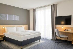 Ein Hotelzimmer mit Bett, Schreibtisch mit Stuhl, Flachbildfernseher und einem Fenster mit Vorhängen.