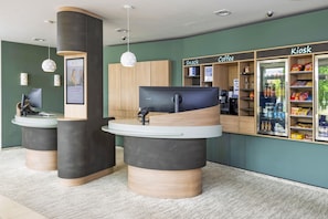 Ein Empfangsbereich mit Theke, Computer und einem Kiosk mit der Aufschrift 'Kiosk Coffee'.