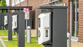 Eine Reihe von Ladestationen für Elektrofahrzeuge im Freien, mit einem Backsteingebäude im Hintergrund.