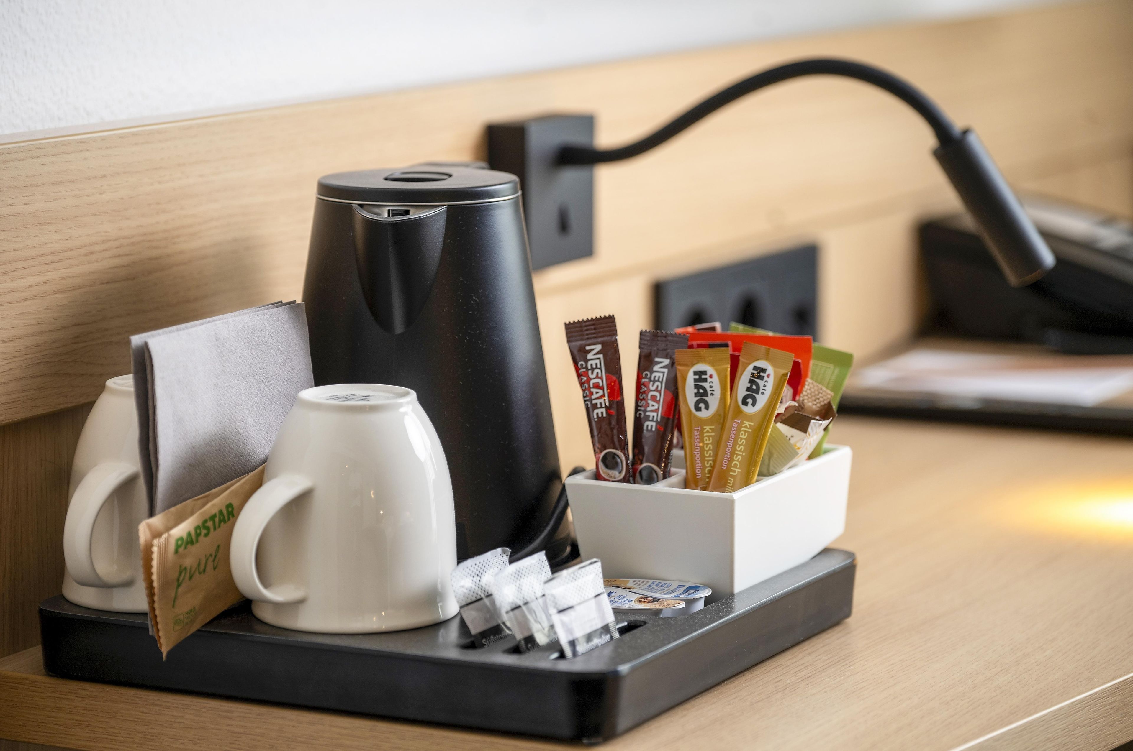 Een koffiehoek met een koffiezetapparaat, een mok en een bak koffiecups.