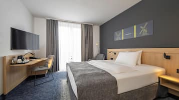 Ein Hotelzimmer mit Bett, Schreibtisch, Stuhl, Fernseher und einem Kunstwerk an der Wand.