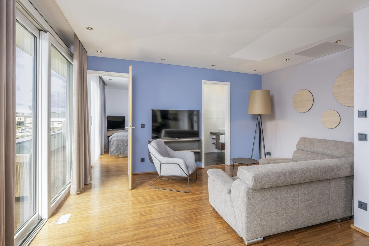 A modern hotel room with a sofa, a chair, a TV, and a mirror.