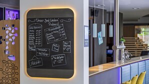 A blackboard with a menu listing restaurant hours and prices, a reception desk, and a bar area with a sign indicating 'Green Key 2026'.