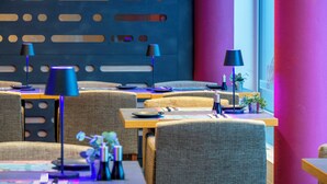 A modern restaurant with multiple tables and chairs, blue and purple lighting, and a decorative wall with cut-out patterns. - Best Western Plus Hotel Papenburg (Papenburg)