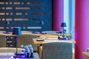 A modern restaurant with multiple tables and chairs, blue and purple lighting, and a decorative wall with cut-out patterns. - Best Western Plus Hotel Papenburg (Papenburg)