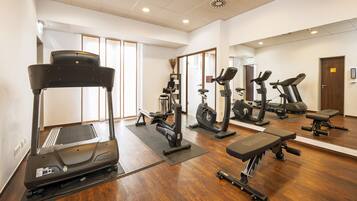 Un gimnasio con diversos equipos de ejercicio, incluyendo cintas de correr, bicicletas estáticas y una máquina de remo.