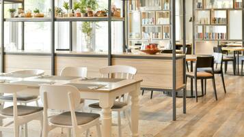 Interior de una cafetería con mesas, sillas, una estantería y un mostrador con vitrina.
