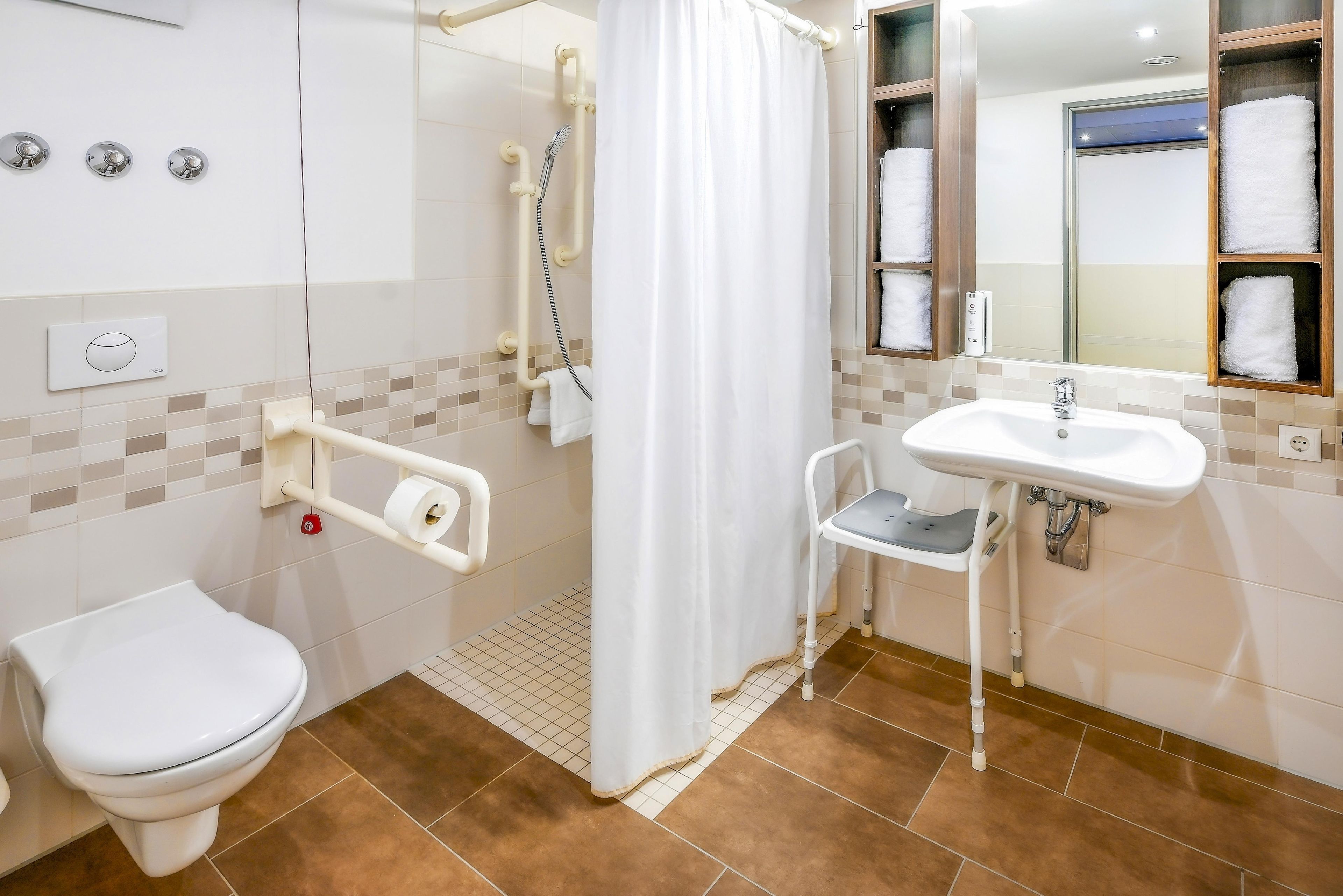 A bathroom with a toilet, a shower with a handheld showerhead, a sink with a mirror, and a towel rack with towels.