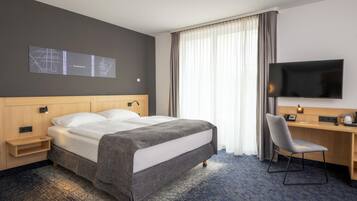Habitación de hotel con cama, escritorio, silla, televisión y ventana con cortinas.