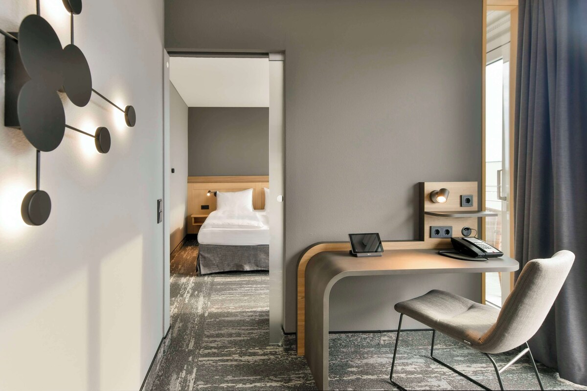 Een hotelkamer met een bed, een bureau met een laptop, een stoel en een aan de muur bevestigde telefoon.
