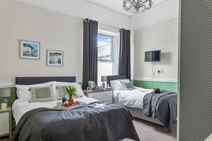 A hotel room with two beds, a television, a window with curtains, and artwork on the walls.