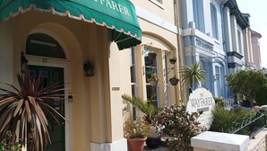 L’entrée d’un hôtel, avec un auvent vert portant l’inscription « WAYFAKER », un panneau indiquant « CHAMBRES LIBRES » et une enseigne « THE WAYFAKER ».