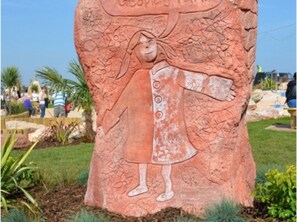 A large stone sculpture of a girl in a dress with a flower pattern, set in a landscaped area with grass and plants. - Wayfarer Guest House (Torquay)