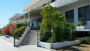 Un bâtiment doté d’un espace extérieur abrité, d’un escalier menant à une porte, ainsi que de diverses plantes et fleurs.