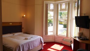 A hotel room with a bed, a desk with a television, and a window with stained glass. - The Old Vicarage Hotel (Leeds)
