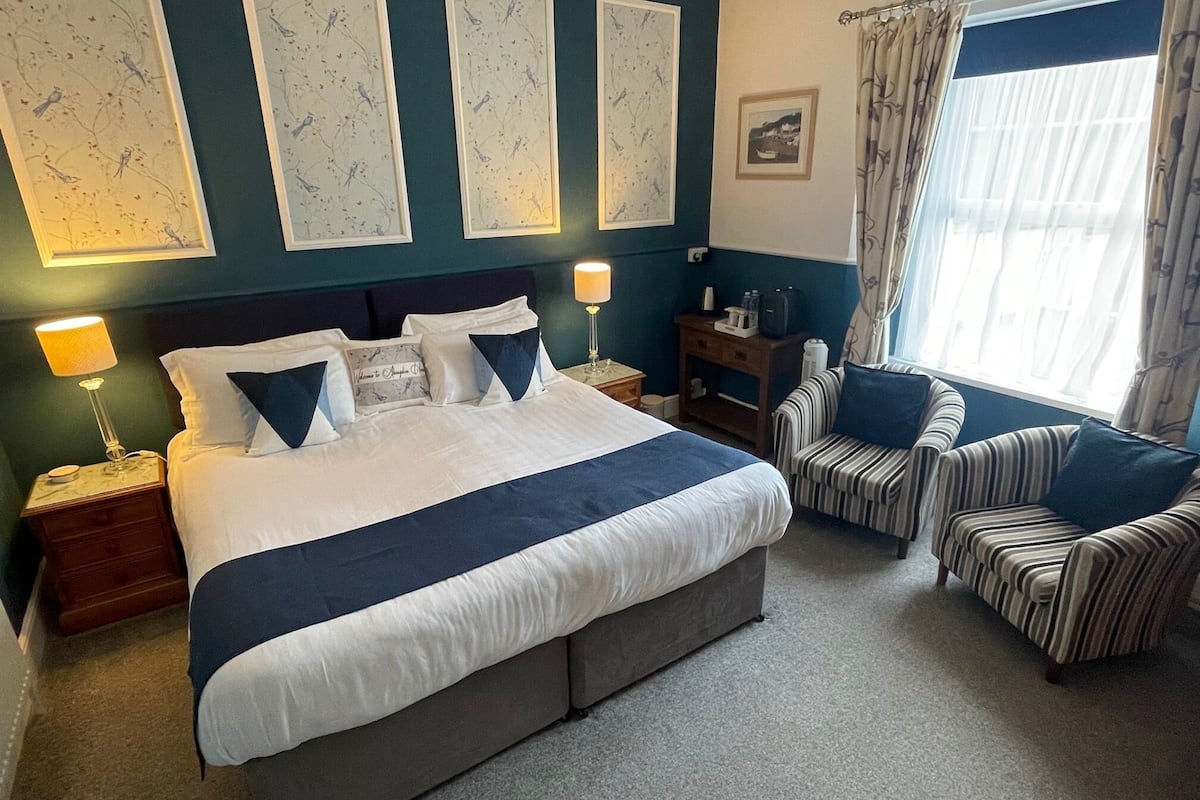 A hotel room with a large bed, two bedside tables, a chair, a small table, and a window with curtains.