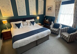A hotel room with a large bed, two bedside tables, a chair, a small table, and a window with curtains. - Abingdon House (Torquay)