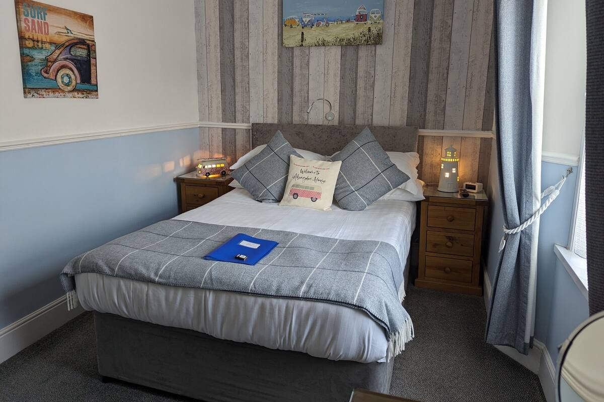 A bedroom with a bed, a nightstand, a lamp, a painting, and a window with curtains.