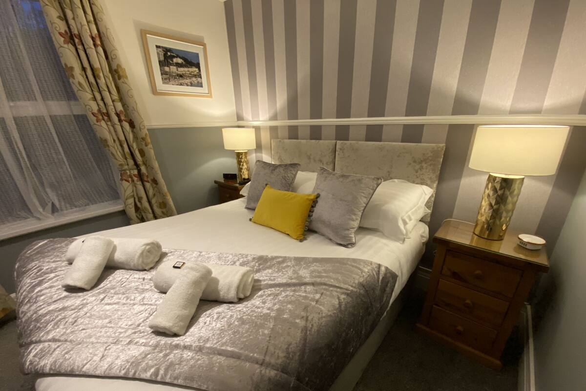 A neatly made bed with towels, a striped headboard, two bedside lamps, and a nightstand with a lamp.