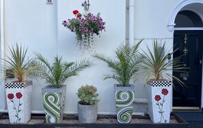 A building facade with a white wall, a black door with the number 104, and a hanging flower basket. - Abingdon House (Torquay)