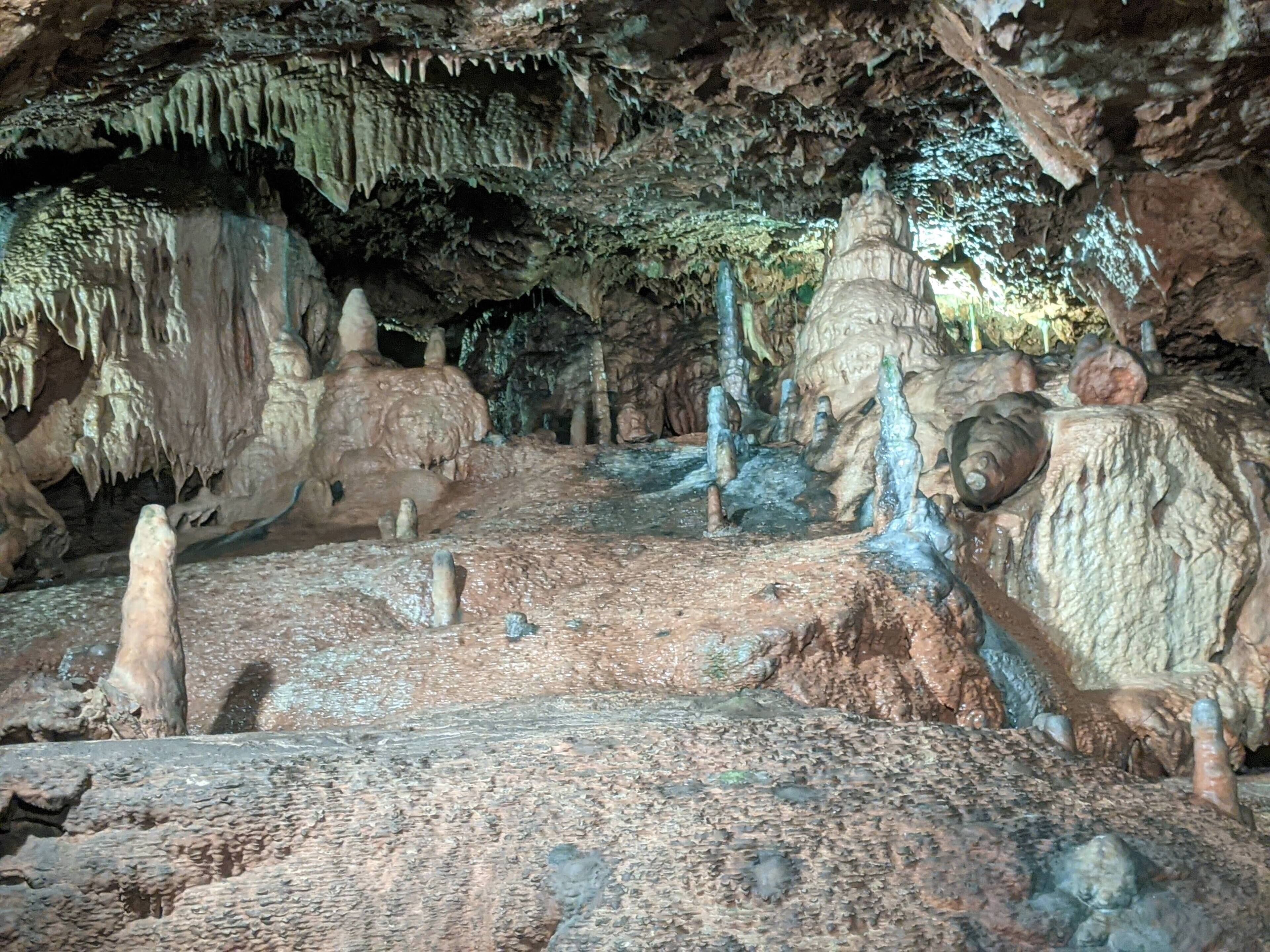 A cave with stalactites and stalagmites, dim lighting, and a rough, uneven floor.