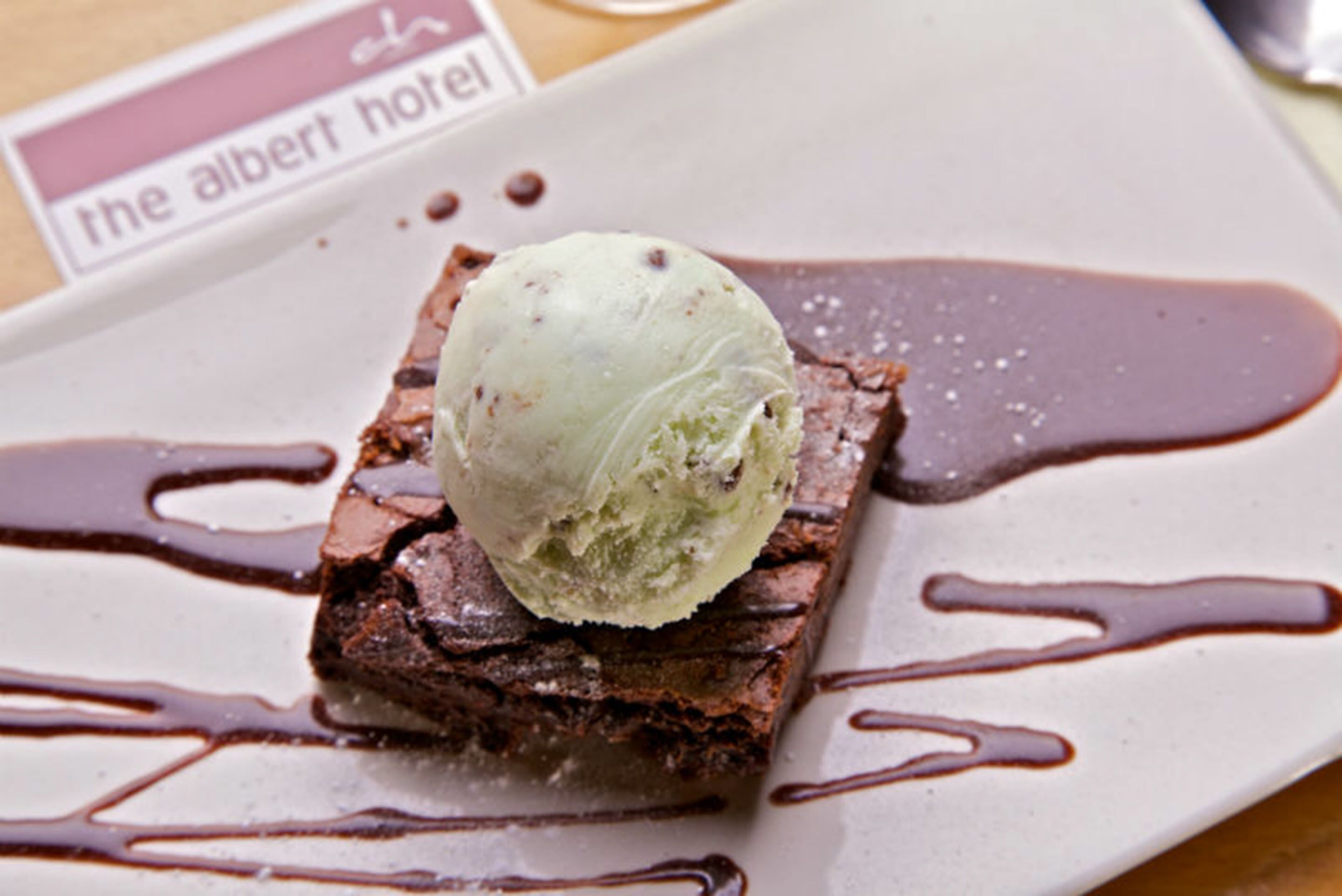 A dessert with ice cream on a brownie, drizzled with chocolate sauce, on a plate with a hotel name card.